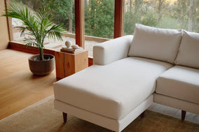 A bright living room with large L-shaped white sofa, plants, and a coffee table full of books.
